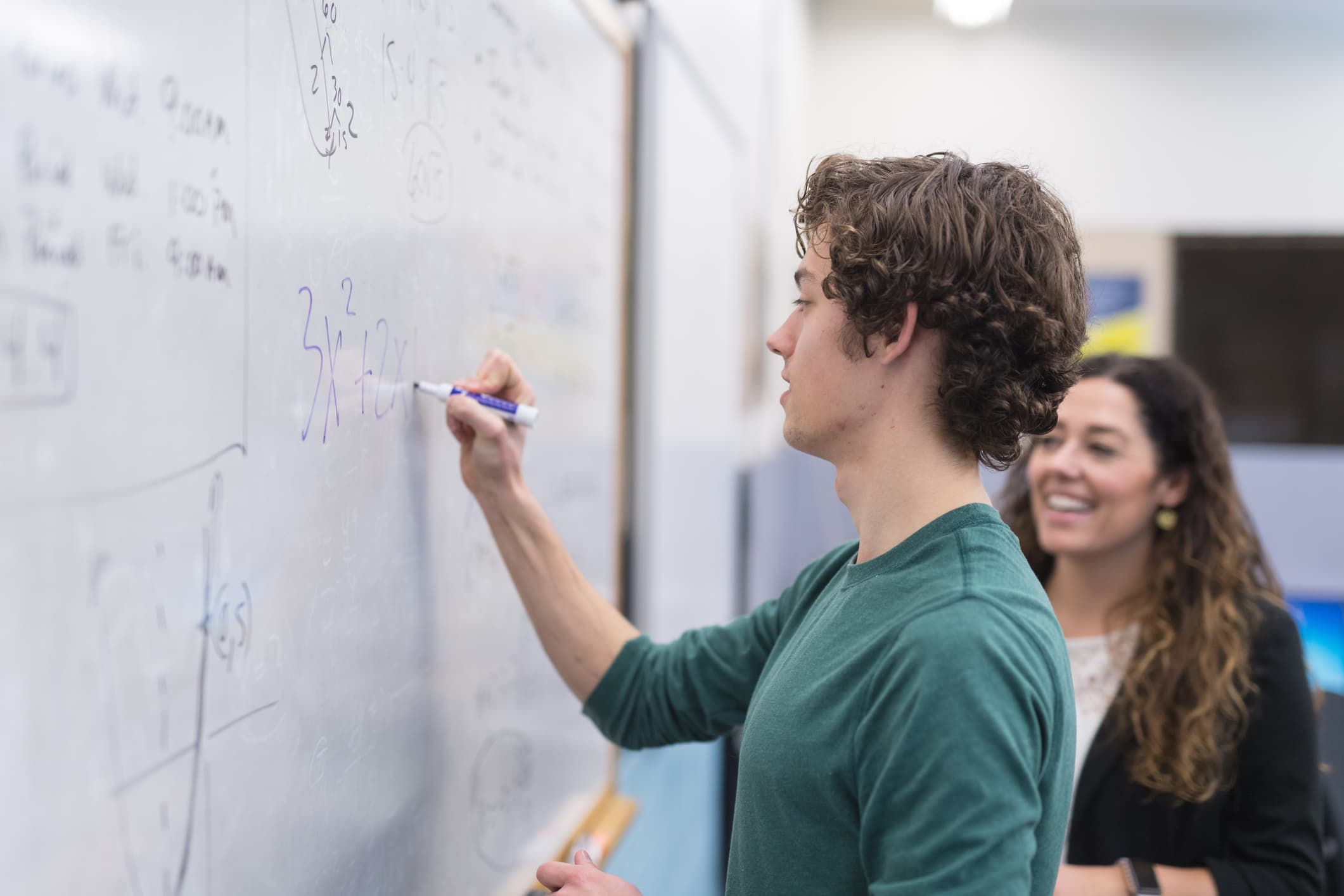 Profesor étnico ayuda a estudiante de secundaria con un problema de matemáticas en la pizarra